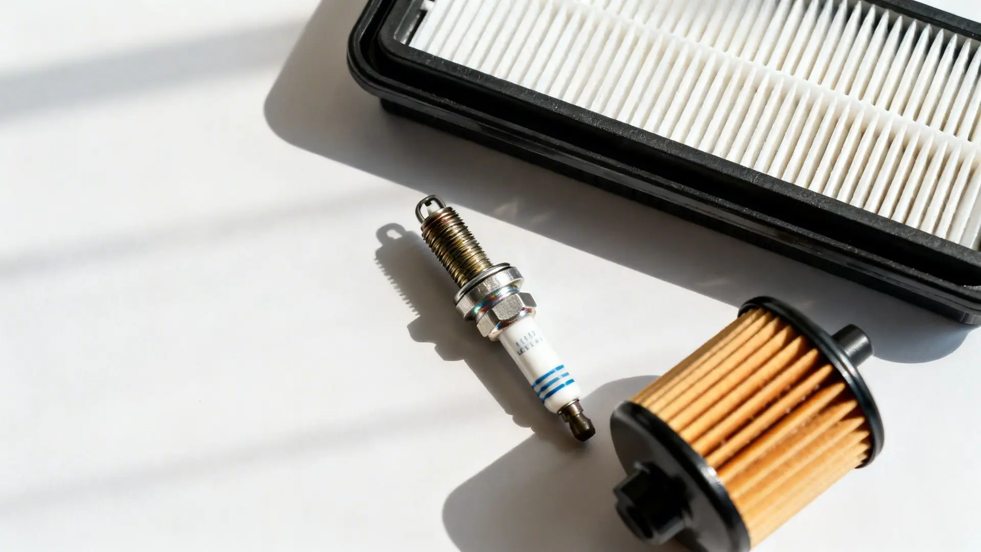 Automotive maintenance parts including an air filter, spark plug, and oil filter on a white background.