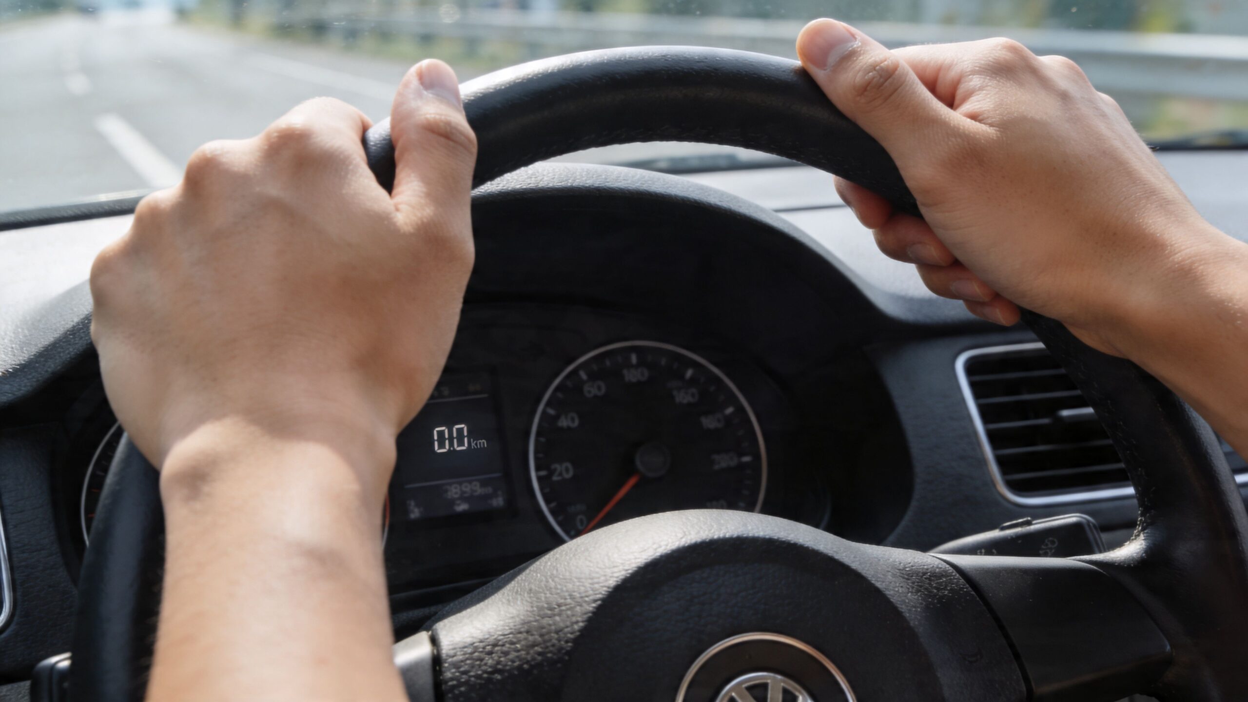 A driver's perspective from behind the steering wheel while driving along an open highway.