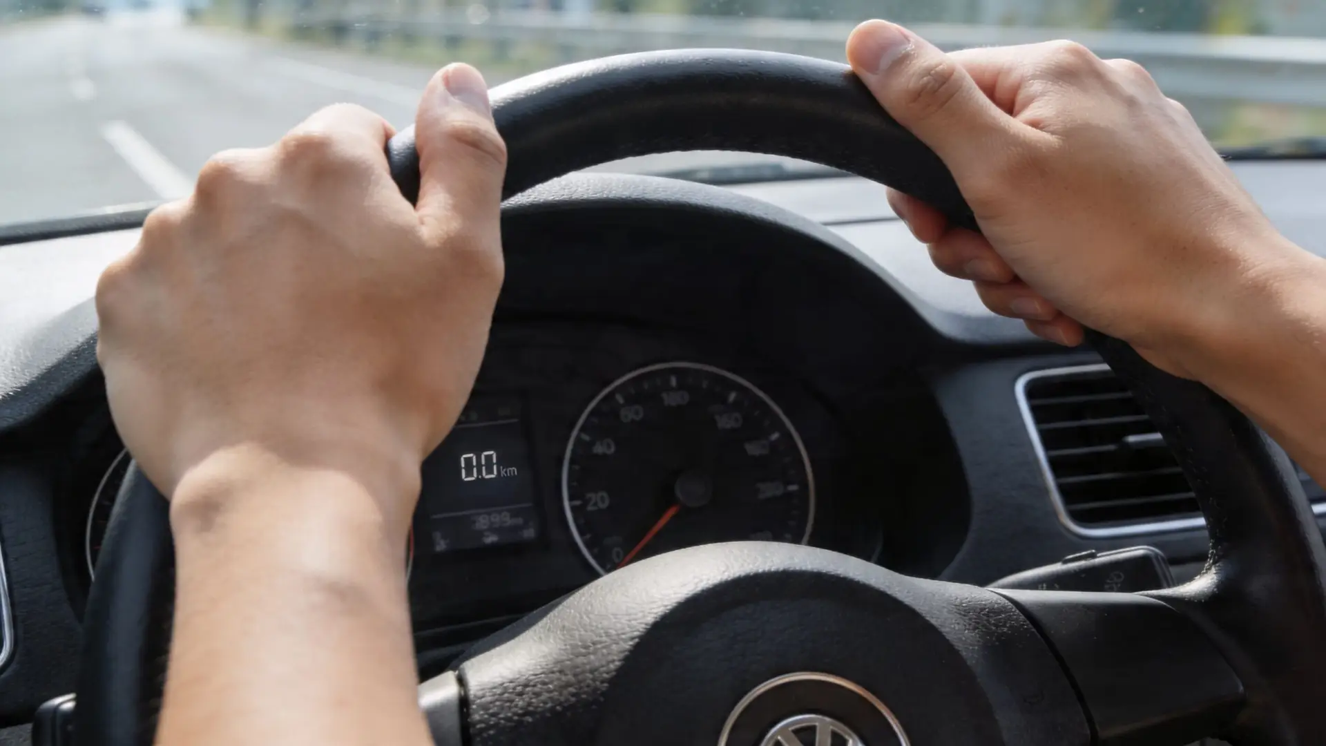 A driver's perspective from behind the steering wheel while driving along an open highway.