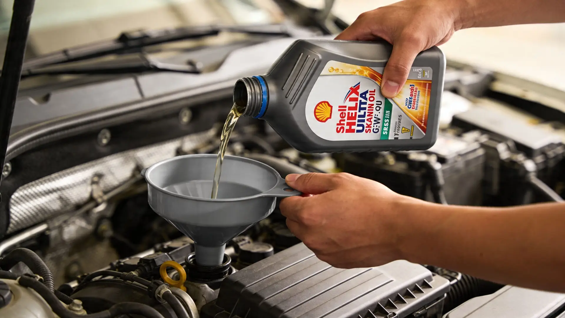 A close-up view of hands pouring Shell Helix motor oil into a car engine using a funnel.