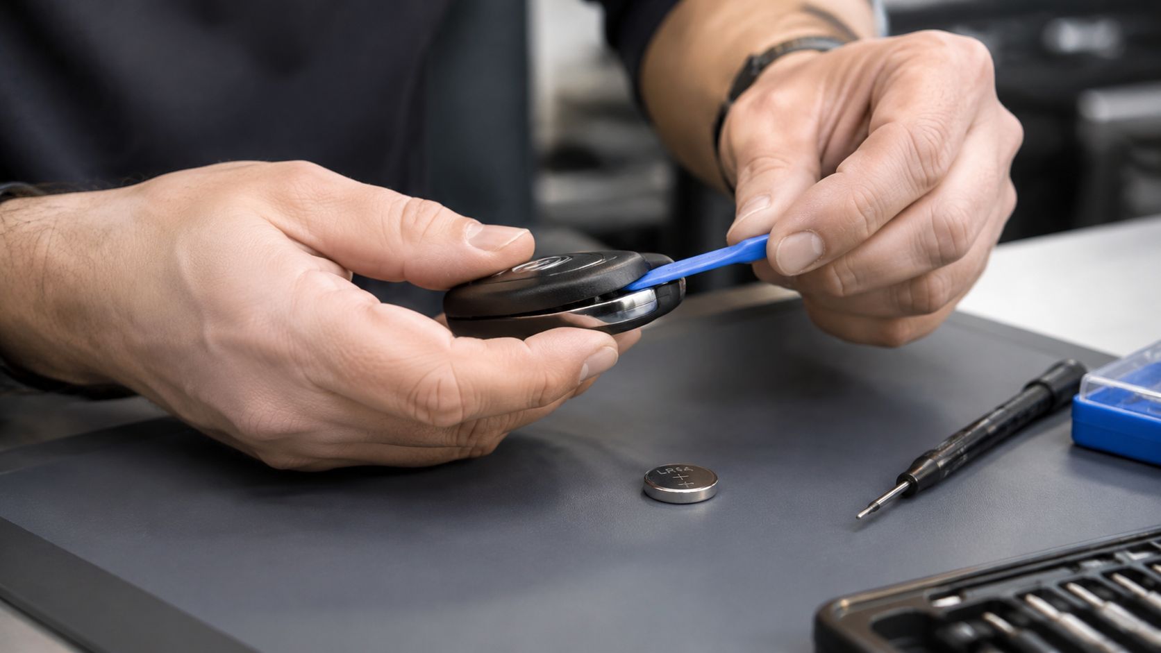 A technician uses a plastic pry tool to open a car key fob for a battery replacement.
