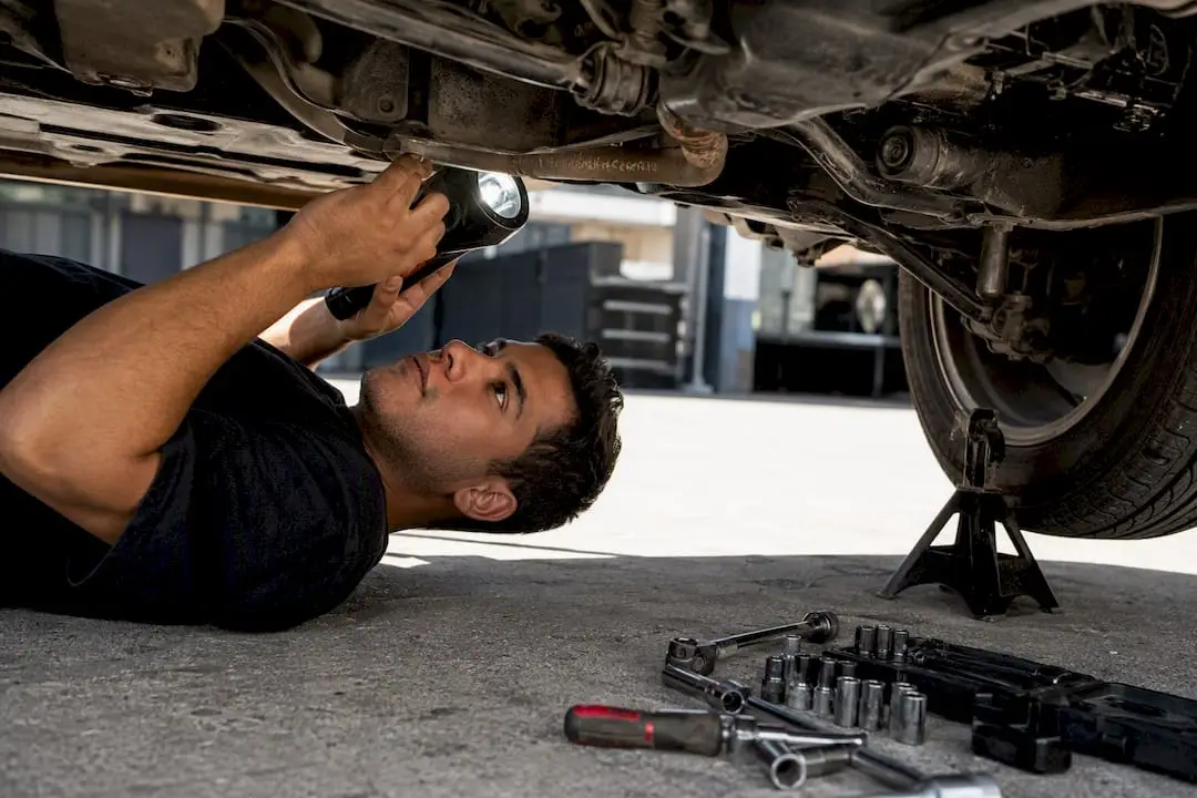 Mechanic inspecting vehicle undercarriage with flashlight