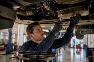 Technician loosening oil pan bolt under car