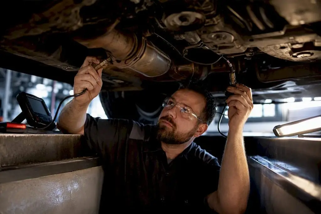 Technician inspecting oxygen sensors beneath vehicle