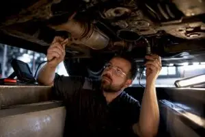 Technician inspecting oxygen sensors beneath vehicle
